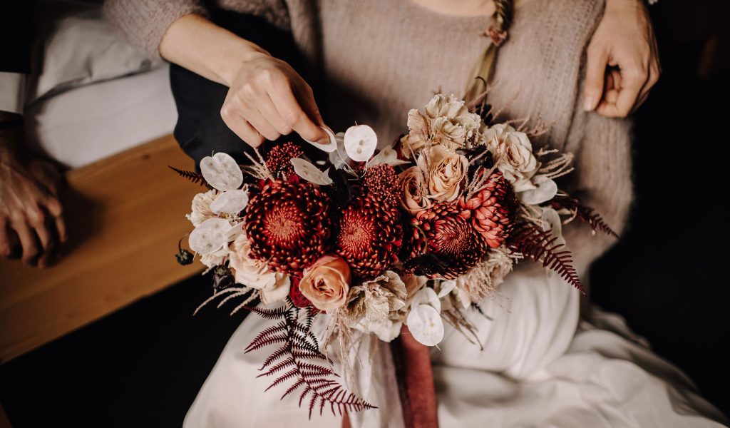 Bridal bouquet with bridal couple in the background at the wedding in the mountains in their wedding location in the Bernese Oberland