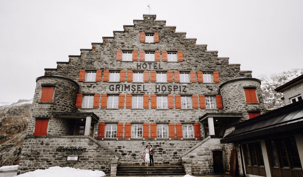 The bride and groom in front of the Berghotel Grimsel Hospiz during their mountain wedding at their wedding venue in the Bernese Oberland in Switzerland